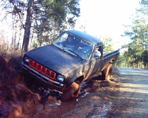 1993 Ford Bronco - A black pickup truck navigates a muddy trail, with its tires deep in the muck.