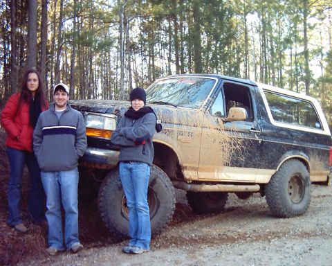 1993 Ford Bronco - A muddy Ford Bronco is parked off-road with three people posing next to it.