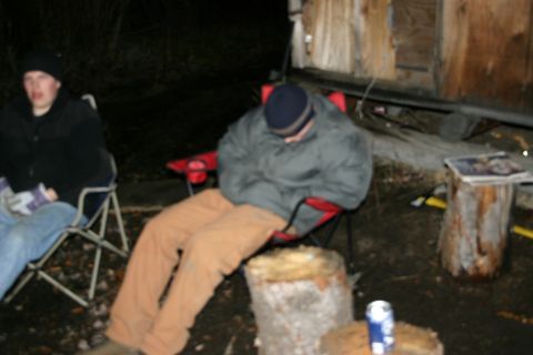 2003 Jeep TJ - Two people relax in camping chairs at night near a rustic wooden building.