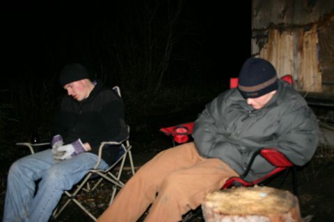 2003 Jeep TJ - Two individuals appear to be resting or sleeping in camping chairs outdoors at night, with a log in the foreground.