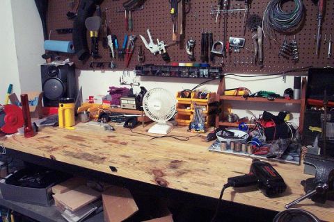 1985 Ford Crown Victoria LTD - A workbench is filled with various tools, electrical components, and a small fan, suggesting a workspace for repairs or projects.