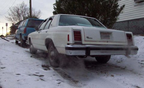 1985 Ford Crown Victoria LTD - White Ford Crown Victoria with a blue pickup truck behind it on a snowy road.