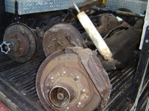 1992 Ford Bronco - Collection of used vehicle brake components and a shock absorber are stored in the back of a pickup truck.