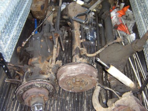 1992 Ford Bronco - Various used vehicle axle and suspension parts are shown in the back of a truck, some with visible rust.