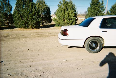 2000 Ford Crown Victoria - Rear view of a white 2000 Ford Crown Victoria parked outdoors on a dirt surface.