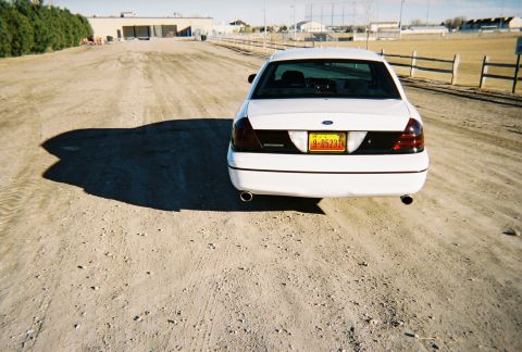 2000 Ford Crown Victoria - Rear view of a white 2000 Ford Crown Victoria on a dirt road with a building in the background.
