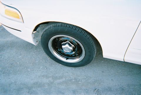 2000 Ford Crown Victoria - Close-up of the front wheel and fender of a white 2000 Ford Crown Victoria.