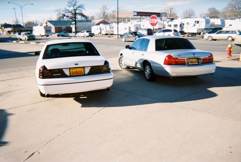 2000 Ford Crown Victoria - Two Ford Crown Victorias are parked side-by-side on a sunny day.