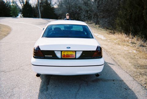 2000 Ford Crown Victoria - A white 2000 Ford Crown Victoria is parked on a road with a person standing behind it.