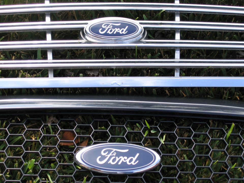 Two Ford grilles on grass: chrome horizontal-bar grille above a dark honeycomb grille, each with blue Ford oval emblem