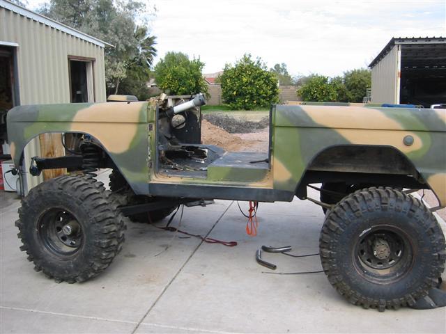 Camo-painted topless full-size SUV project on a lift with mud tires, side view