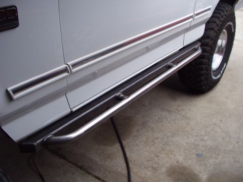 1993 Ford Bronco - Custom rock sliders are mounted to the side of a white vehicle, with a close-up view of the tubing and the vehicle's tire.