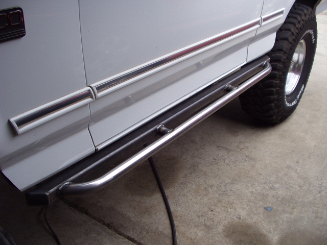 White Bronco lower side with chrome tubular rock slider step bar and mud-terrain tire