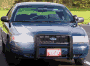 1998 Ford Crown Victoria - A dark blue police car is seen from the front, equipped with a push bar and a light bar on the roof.