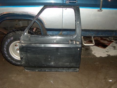 1986 Ford Bronco - A detached vehicle door is shown next to the wheel well of a blue truck.