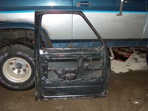 1986 Ford Bronco - A detached car door is placed next to a blue and silver vehicle, revealing its internal structure and a tire.