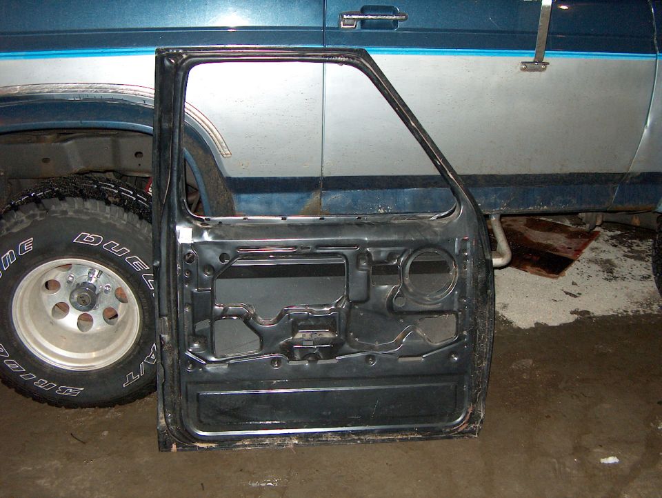 Stripped inner panel of a removed truck door leaning beside a two-tone blue truck