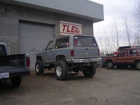 1984 Ford Bronco II - Modified 1984 Ford Bronco II sits outside a fabrication shop next to other vehicles.