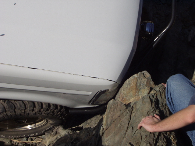 Lower front fender and tire of a white Bronco against a boulder, person spotting