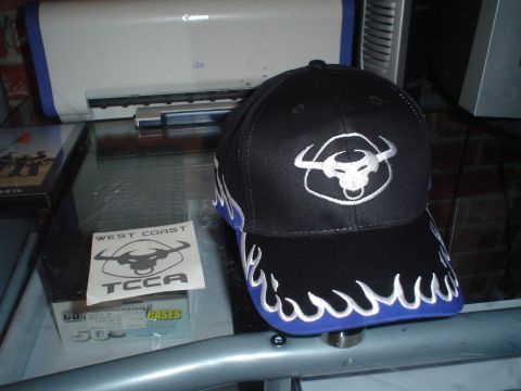 1993 Ford Taurus - A black baseball cap with a bull logo and flame accents sits on a glass table next to a sticker and a printer.