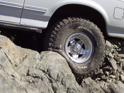 1993 Ford Bronco - A white SUV navigates a rocky terrain, its BFGoodrich Mud-Terrain tires gripping the stones.