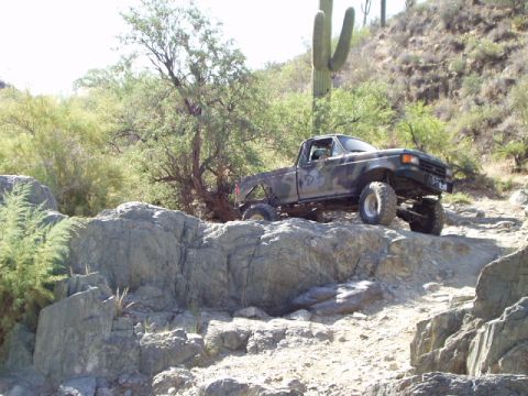 1993 Ford Bronco - A lifted Ford pickup truck navigates a rocky desert trail under a bright sky.