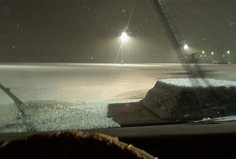 1985 Ford LTD Crown Victoria - View from inside a vehicle looking out at a snow-covered parking lot at night, with streetlights illuminating the scene.