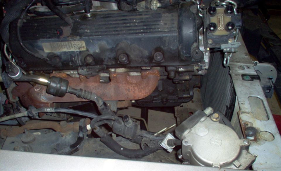 Side view of an engine with black valve cover and rusty exhaust manifold in an engine bay