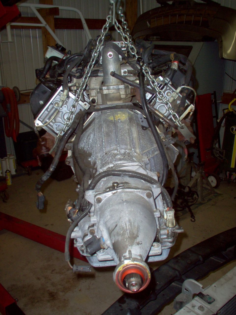 V8 engine and transmission hanging from chain in a garage, transmission end facing camera