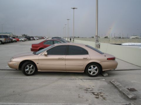 1997 Mercury Sable - A tan 1997 Mercury Sable is parked in a lot with other vehicles under a cloudy sky.
