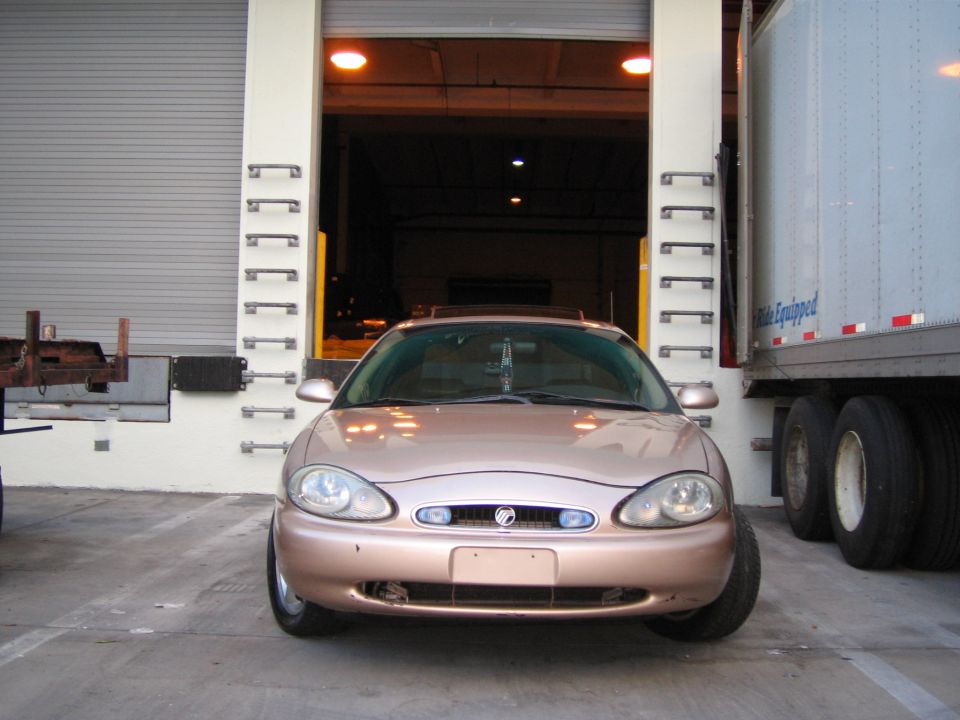 1997 Mercury Sable, rose gold, parked facing forward in front of a loading dock with a semi-trailer to its right