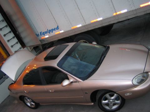 1997 Mercury Sable - A tan sedan with dual sunroofs is parked next to a large semi-trailer, with its trunk open.