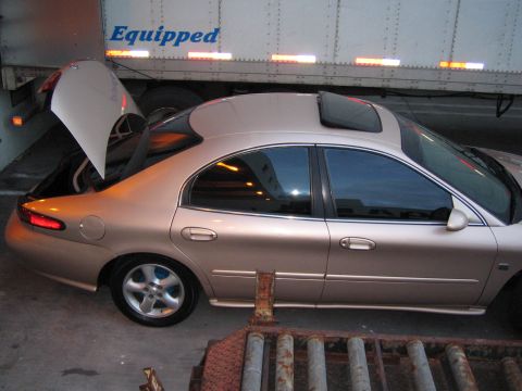 1997 Mercury Sable - A tan sedan with its trunk and sunroof open is parked next to a large trailer with the word "Equipped" on its side.