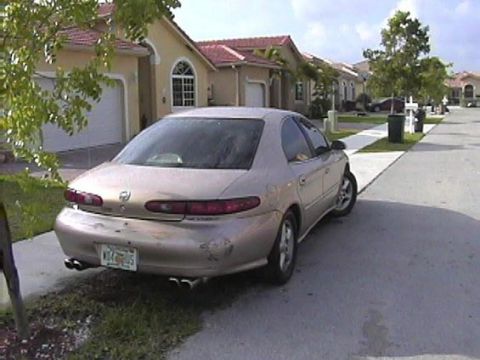 1997 Mercury Sable - A gold sedan is parked on a residential street, showing its rear end and license plate.