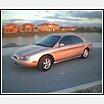 1997 Mercury Sable - A gold 1996 Mercury Sable sedan is parked on a paved surface with houses and a body of water in the background.