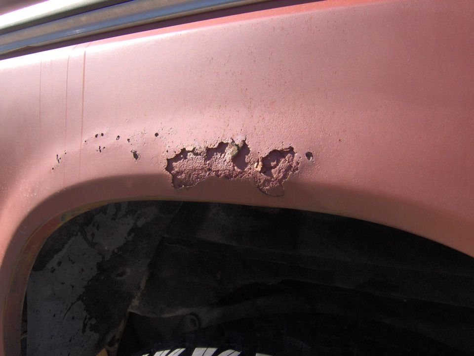 Rust holes and bubbled paint on red quarter panel above wheel arch of a 1978 Ford Bronco