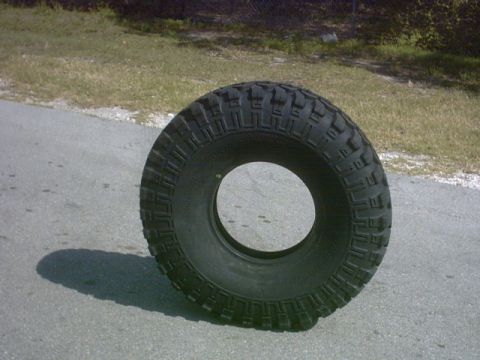1992 Ford Bronco - A single off-road tire is shown resting on a paved surface with grass in the background.