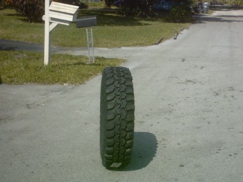 1992 Ford Bronco - A single off-road tire is shown on a paved surface, casting a shadow.