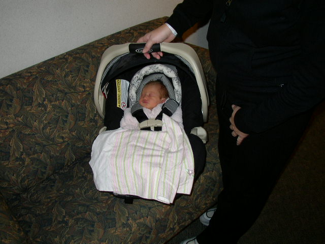 Baby sleeping in a Graco car seat on a patterned couch, held by a person