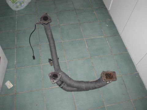 1993 Mazda MX-6 - An exhaust manifold with an attached oxygen sensor lies on a tiled floor.