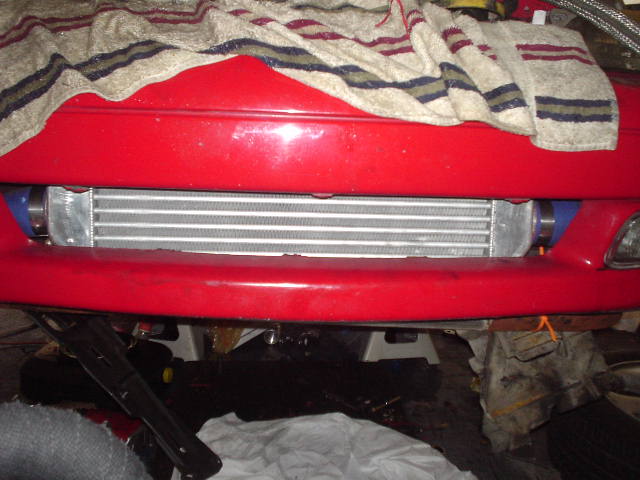 Front-mount intercooler installed behind the bumper of a red car in a garage