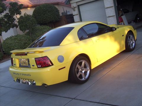 2002 Ford Mustang - A yellow Ford Mustang is parked in a driveway, showing its rear end and custom exhaust tips.