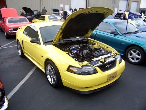 2002 Ford Mustang - A yellow Ford Mustang is parked with its hood open, revealing the engine bay.