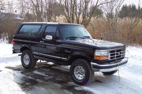 1995 Ford Bronco - This black 1995 Ford Bronco is shown in a three-quarter front view, parked on a snowy surface with trees in the background.