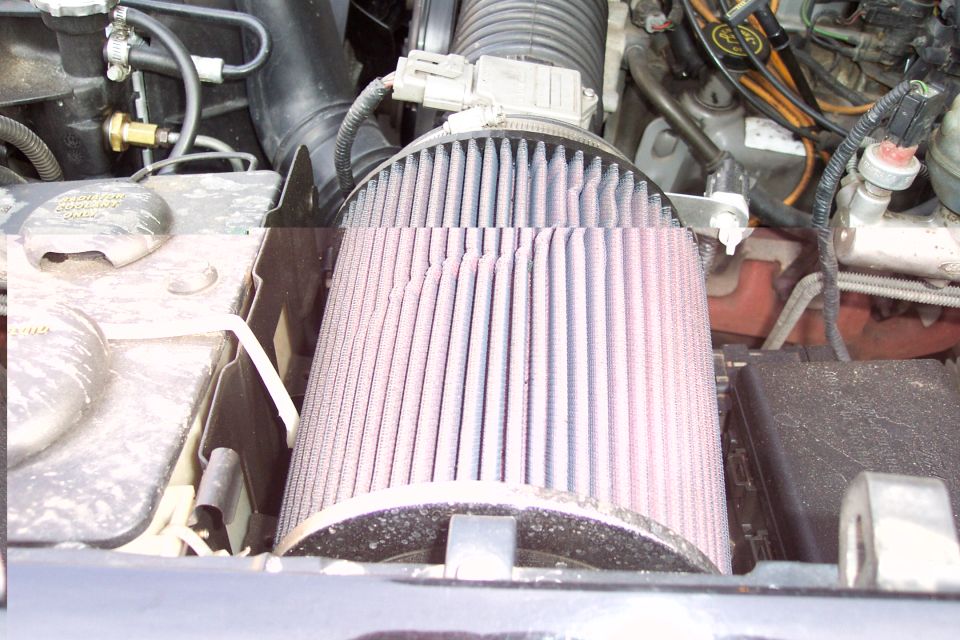 Conical red oiled air filter mounted in a dusty engine bay with wiring and ducting
