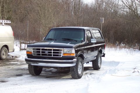 1995 Ford Bronco - A black Ford Bronco is parked in a snowy area next to a tan van.