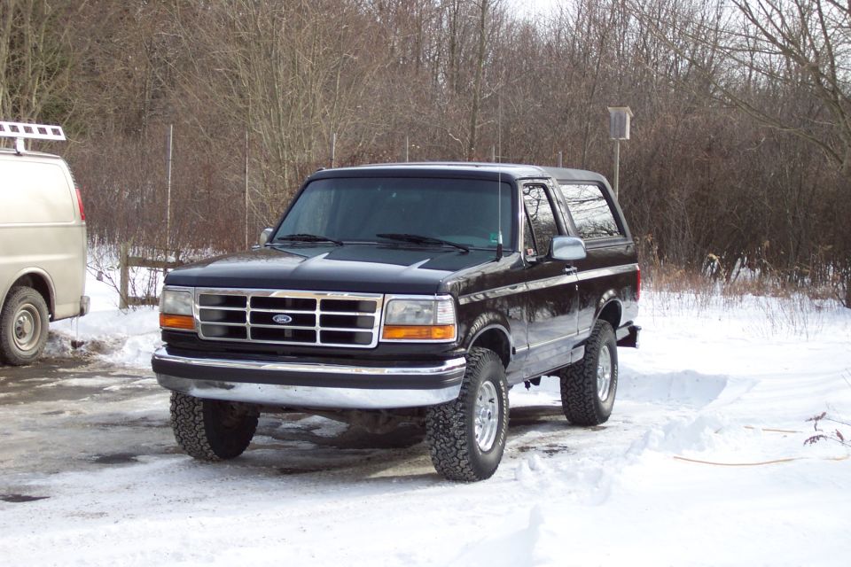 Black Ford Bronco parked in snow, with a tan van to its left