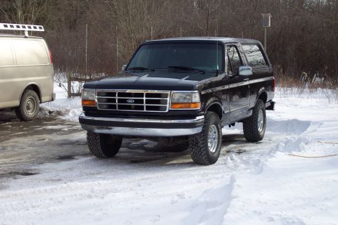 1995 Ford Bronco - A black Ford Bronco is parked in a snowy area next to a van.