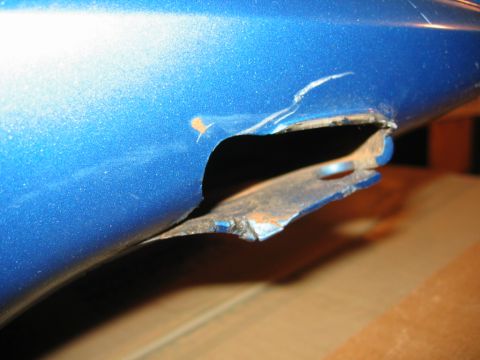 1985 Ford LTD Crown Victoria - The blue car panel has a significant dent and a hole, revealing rust underneath the paint.