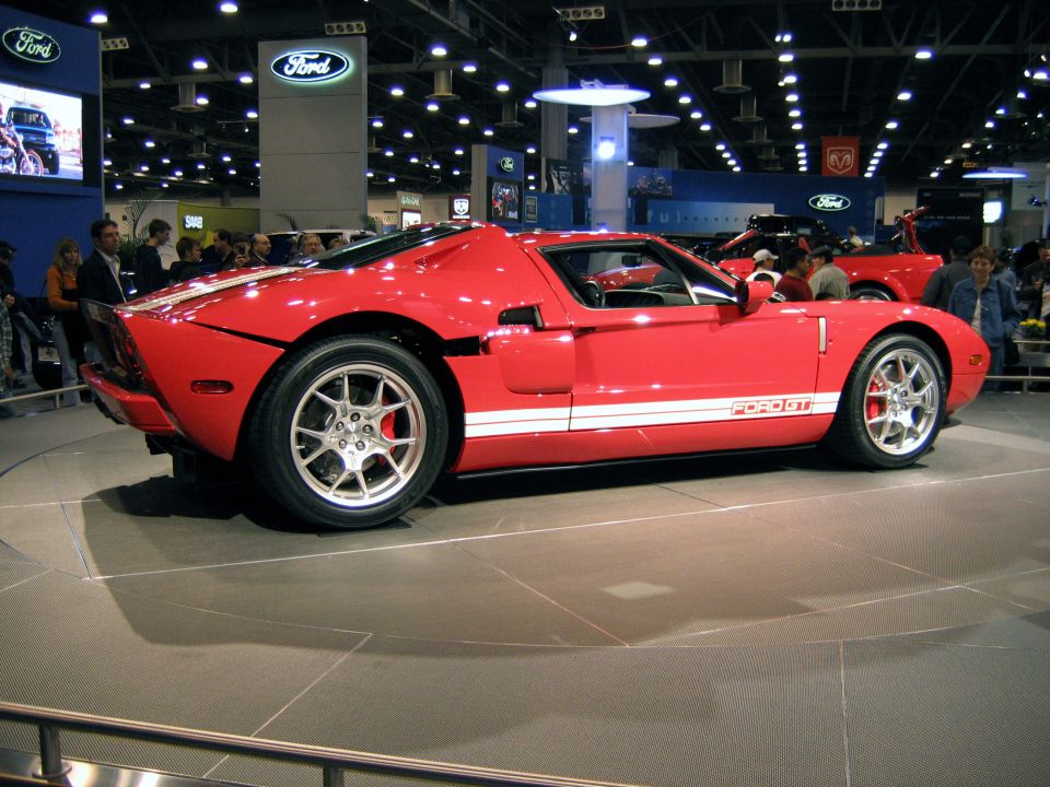 Red Ford GT with white stripes, side profile on a turntable at an auto show